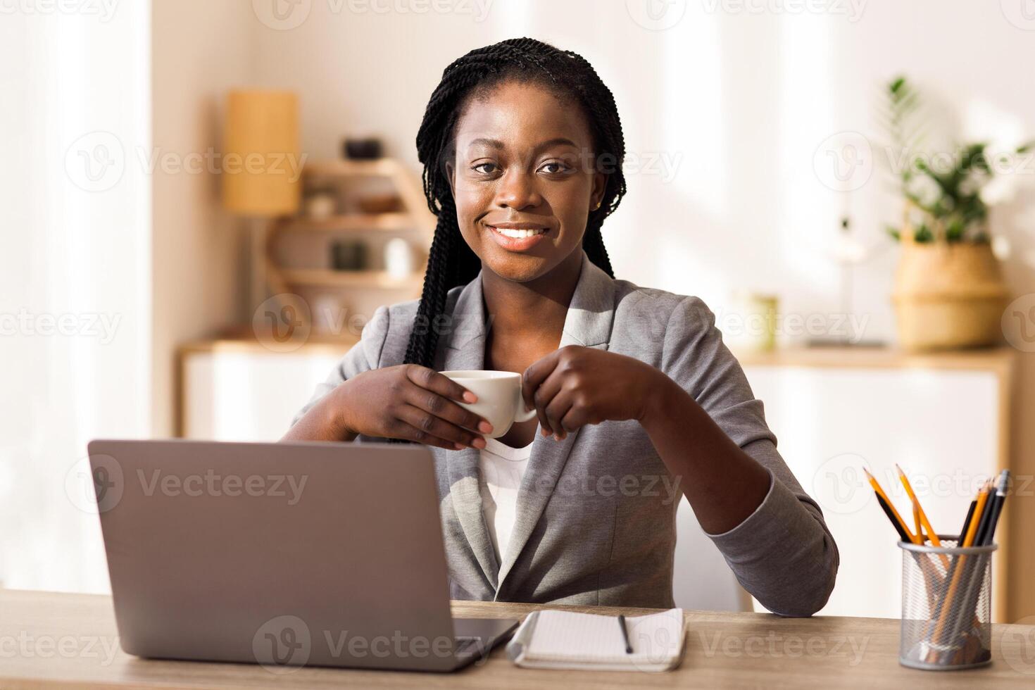 Millennial employee. Smiling black secretary drinking coffee at workplace in modern office and looking at camera, copy space photo