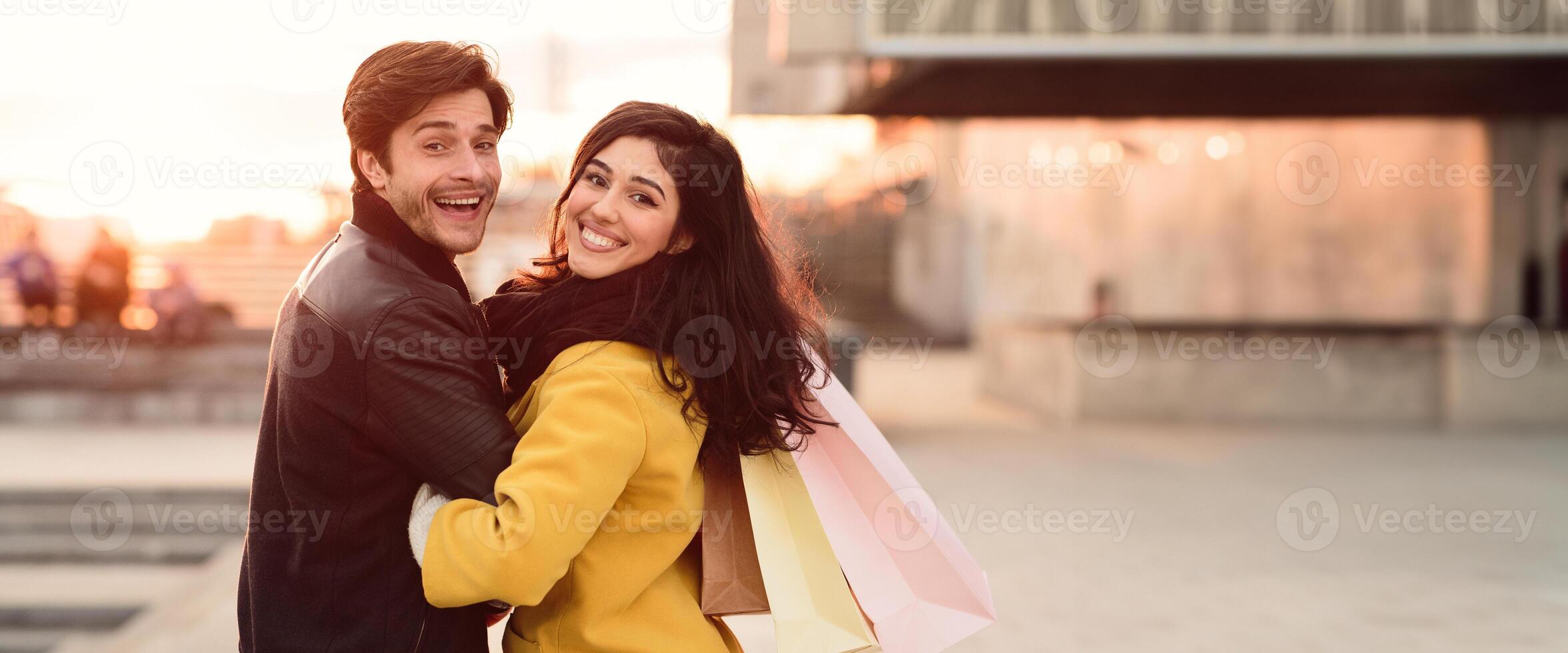 A couple smiles while walking with shopping bags in hand, enjoying their time on a bustling city street in autumn, copy space photo