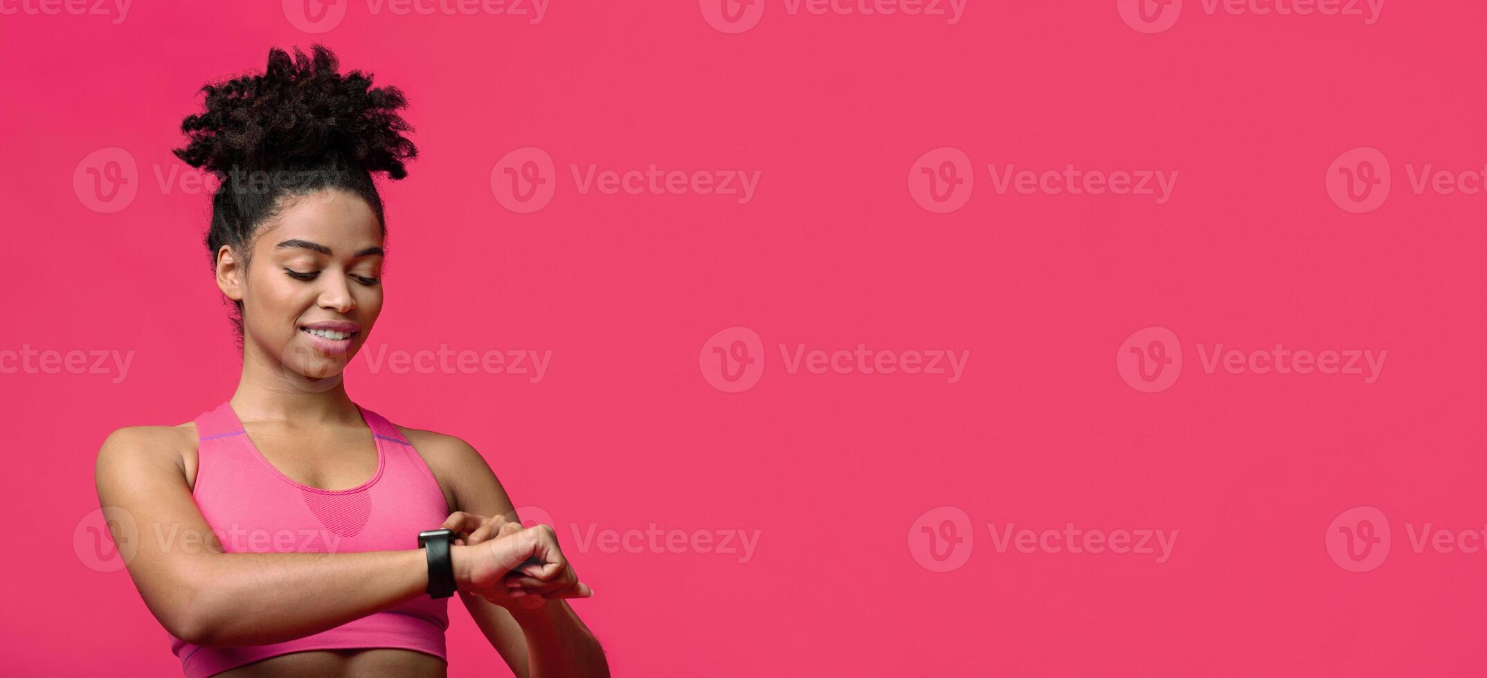 Fitness afro girl using activity tracker smartwatch as heart rate monitor for workout or tracking her weight loss improvement, red background, fitness tracker, free space photo
