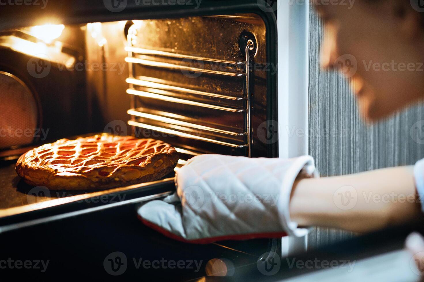 Homemade baking. Happy housewife taking fresh pie out of oven at home photo