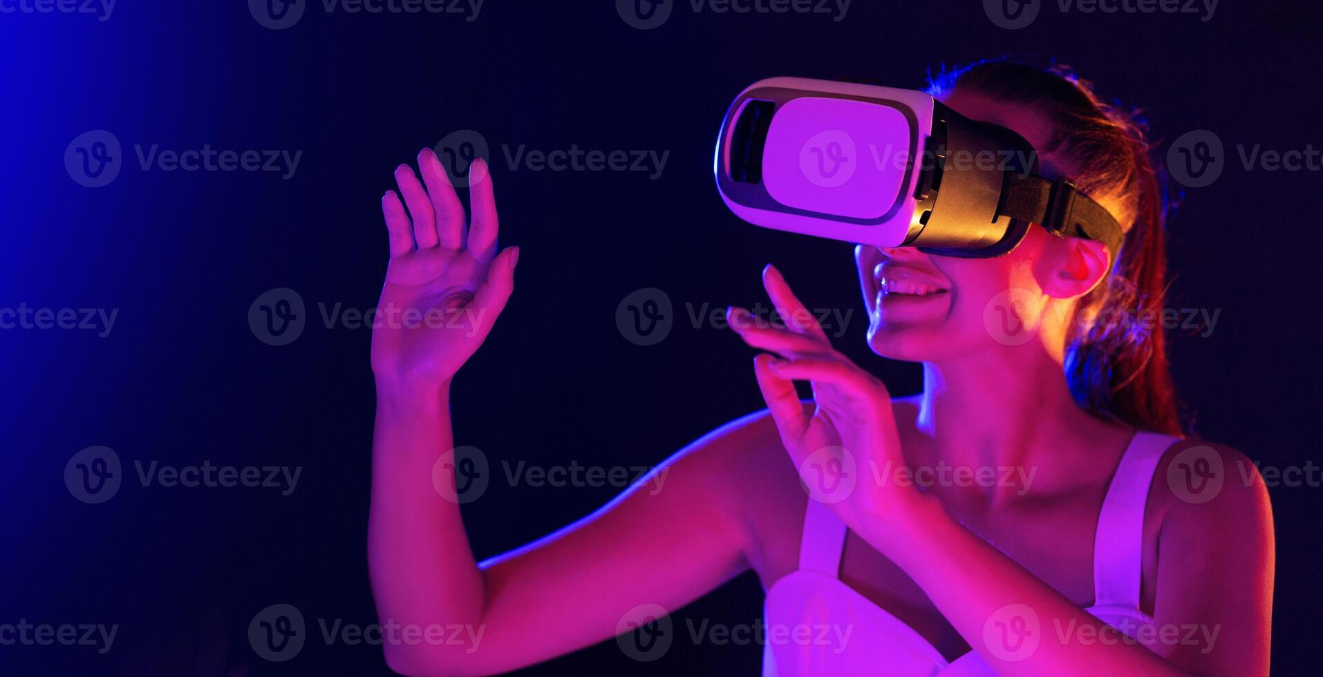 A woman wearing a virtual reality headset, exploring a digital environment while immersed in the virtual experience in dusk. She is interacting with the technology photo
