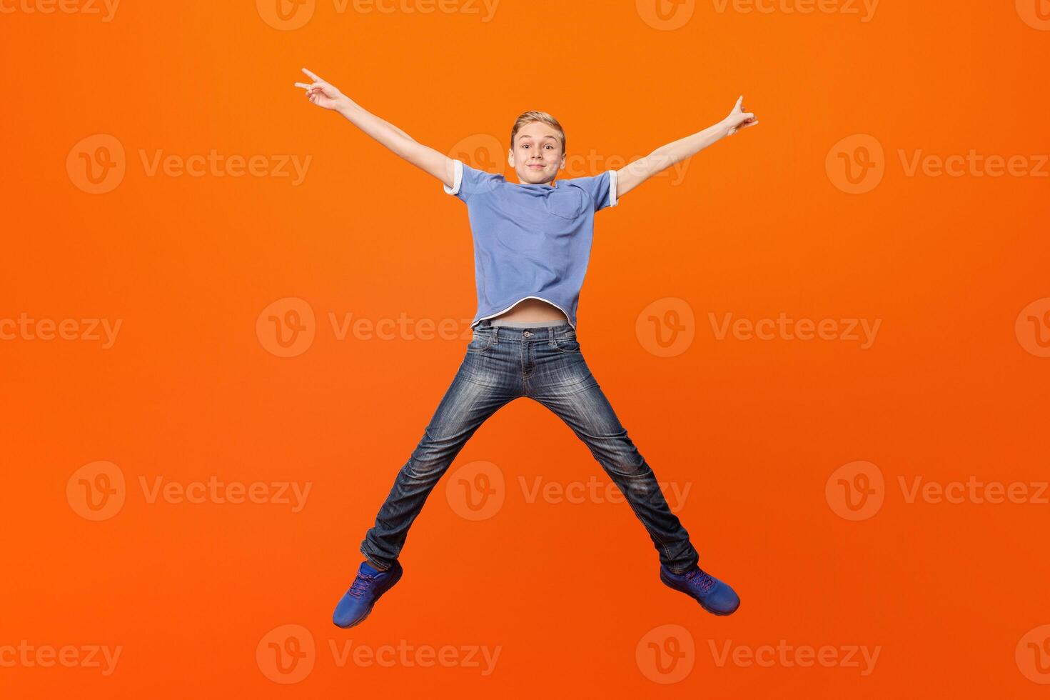 Happy school boy having fun, jumping on orange studio background photo