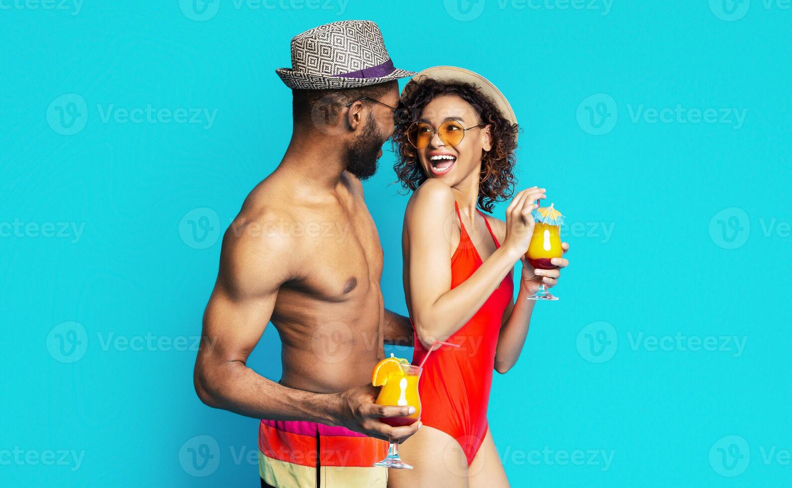 African American couple in summer attire, smiling and enjoying cocktails together against a bright blue background. Both are holding colorful drinks and appear to be happy and relaxed. photo
