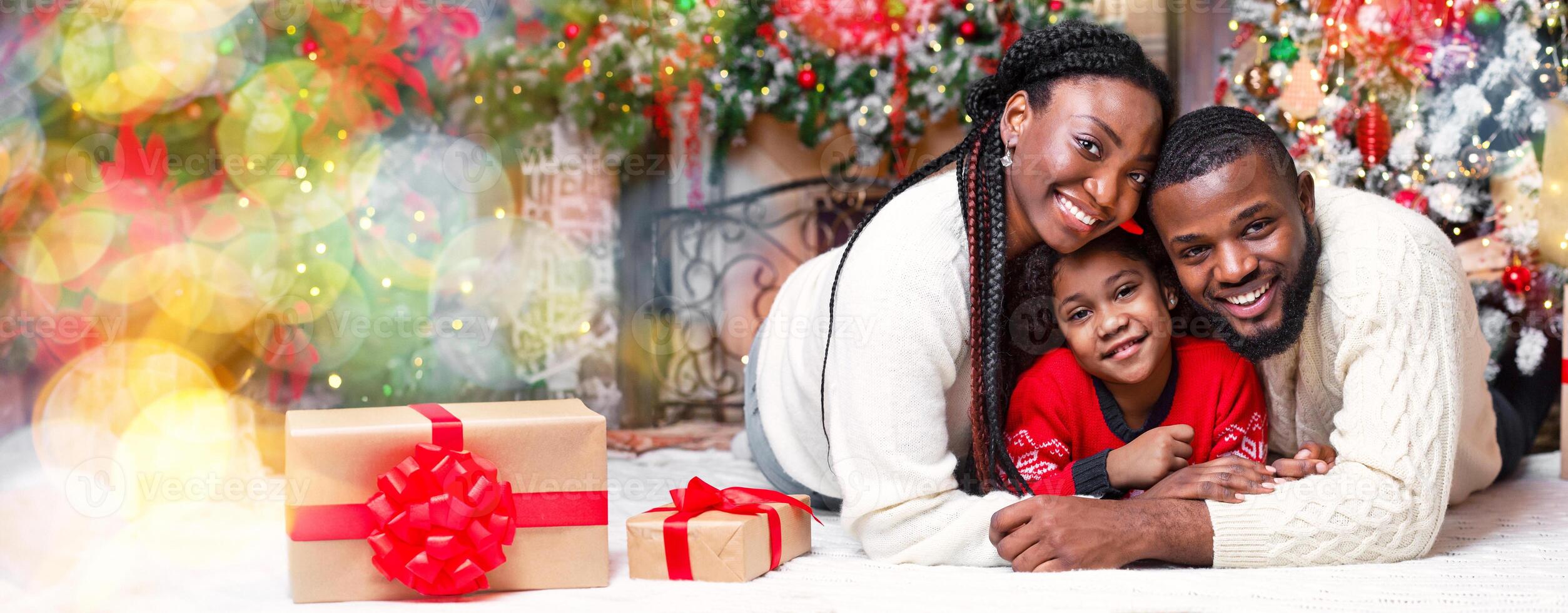 Portrait of happy african american family on Christmas Eve, lying on floor near Xmas tree, cuddling and smiling at camera photo