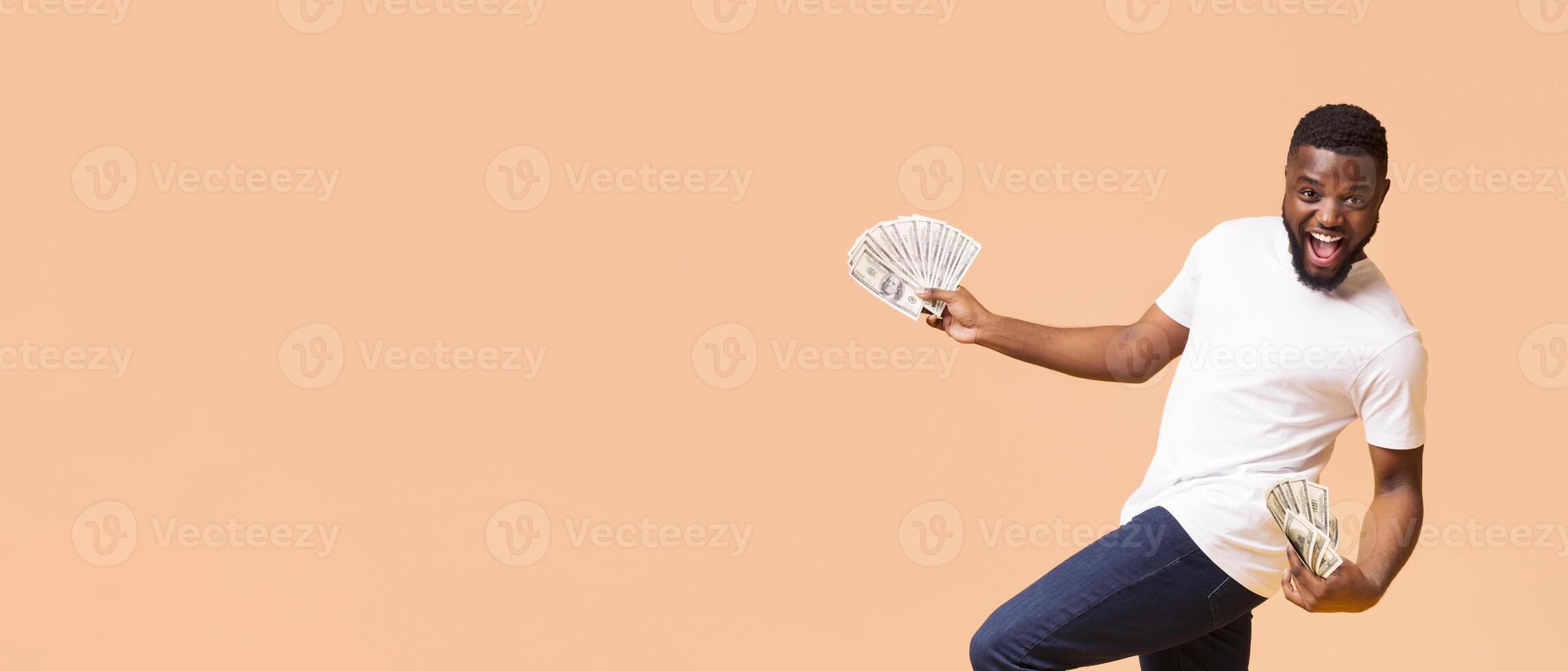 A happy young black man with short black hair is standing in front of a peach-colored background, panorama with copy space photo