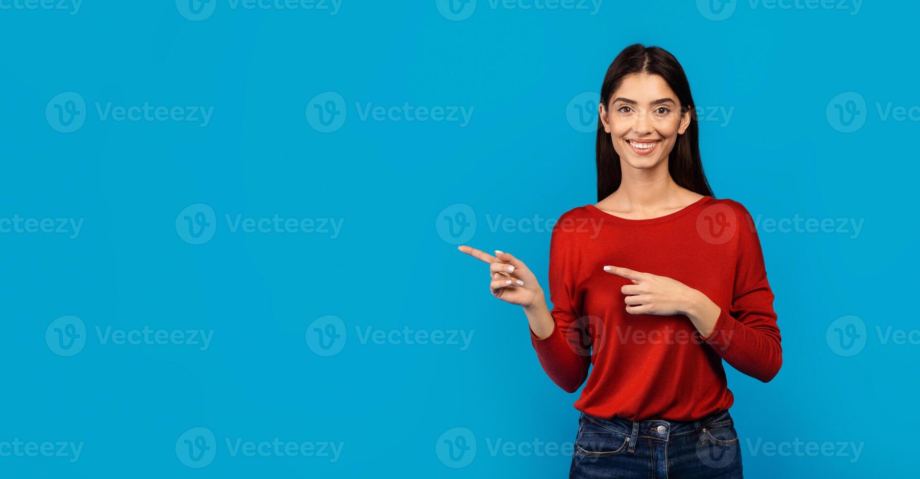 A woman wearing a red sweater is pointing at an unseen object off-camera, engaged and focused on whatever has caught her attention, her gesture suggesting significance or direction, copy space photo