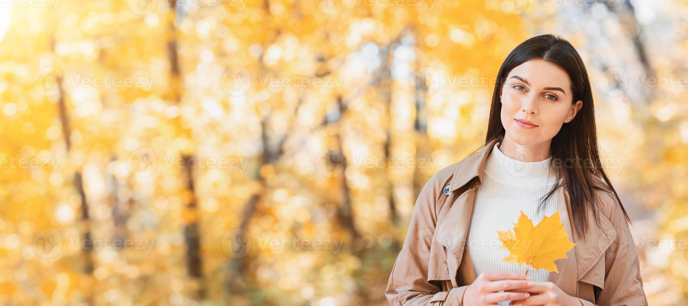 Portrait of pretty woman with yellow marple leaf posing in autumn forest, copy space photo