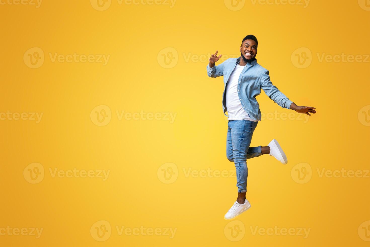 Portrait of funny black man jumping on yellow background with euphoric face expression, free space for text photo