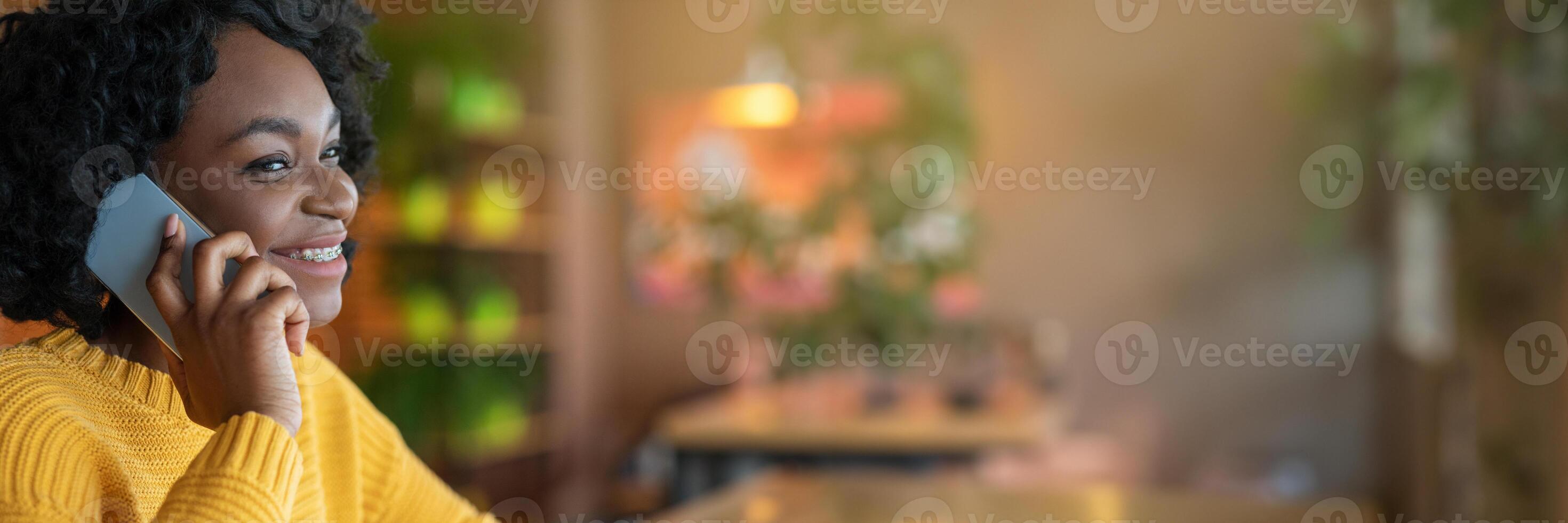 Side view of young african american young woman talking by modern smartphone, cafe interior, close up, panorama with copy space photo