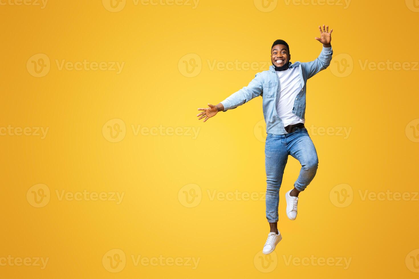 Cheerful millennial black guy having fun, jumping in air on yellow background, free space photo