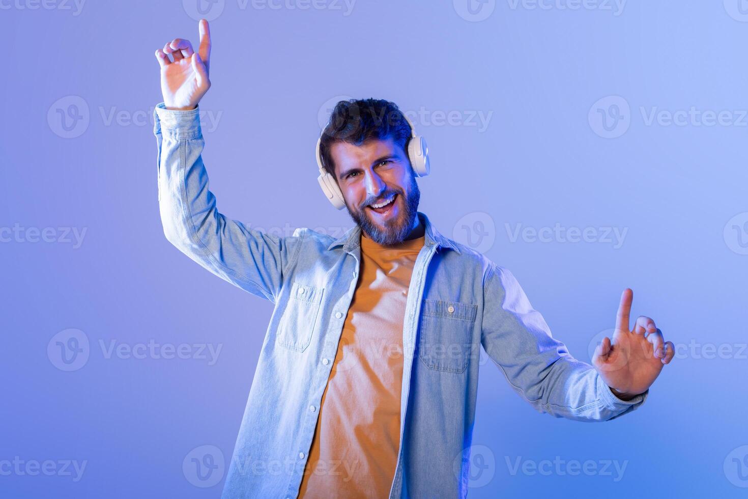 A young man enthusiastically dances to music, wearing headphones, in a vibrant, colorful room during nighttime. He looks happy and energetic. photo