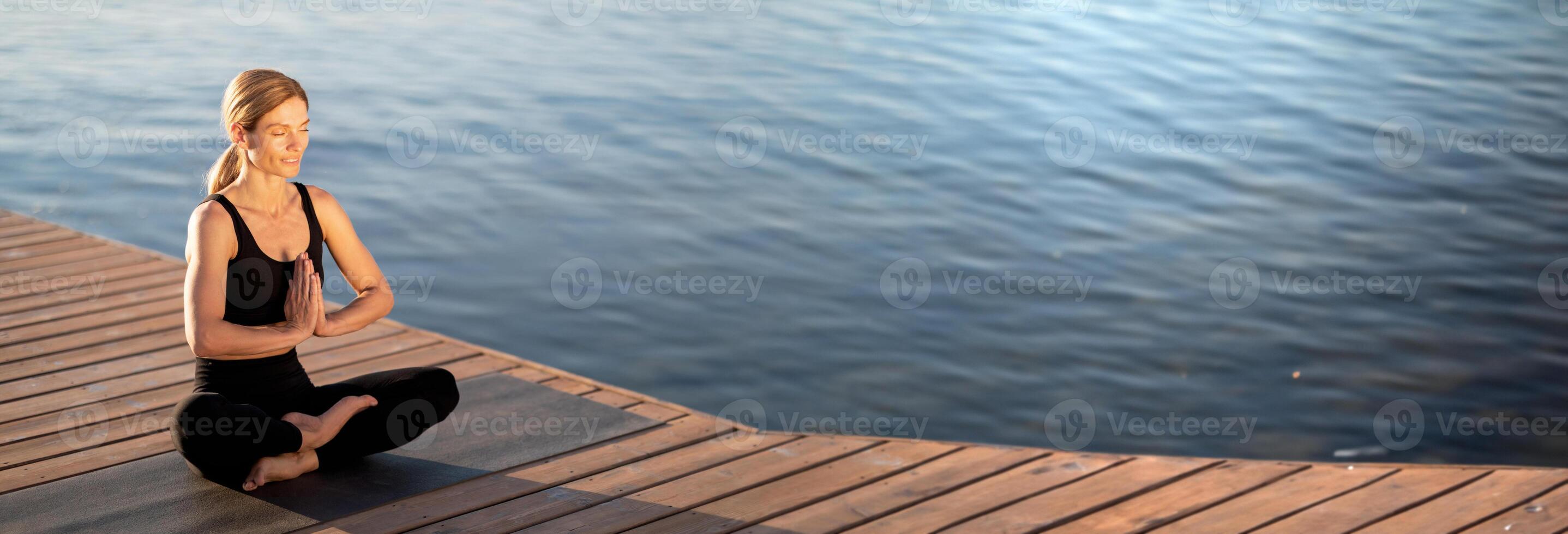 Morning Meditation. Calm Middle Aged Woman Meditating Outdoors On Wooden Pier, Relaxed Beautiful Lady Sitting With Closed Eyes In Lotus Position, Practicing Yoga Near The Sea, Copy Space photo