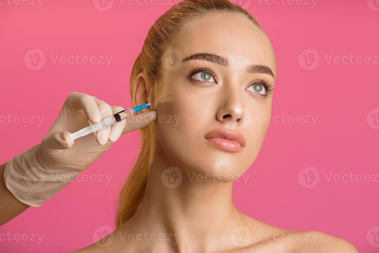 A close-up photo of a woman receiving a facial injection treatment. The woman is looking up and has a serious expression. The injection is being administered by a gloved hand
