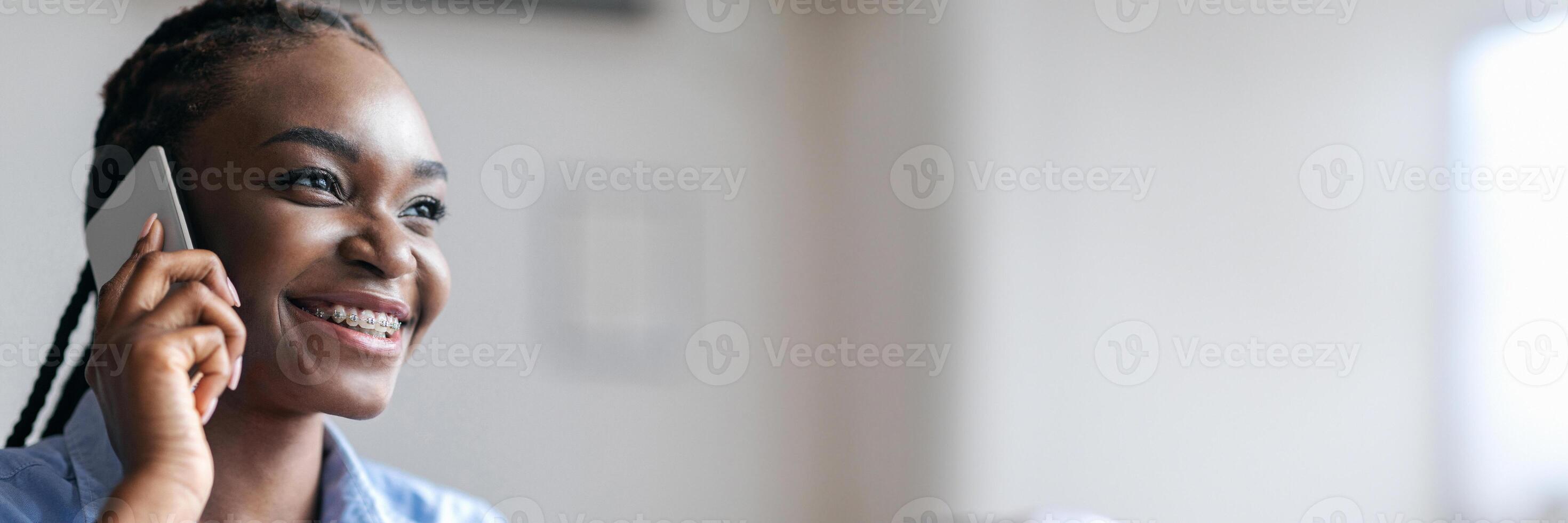 Phone Call. Closeup portrait of cheerful black woman talking on cellphone, enjoying conversation, having braids and brackets, copy space photo