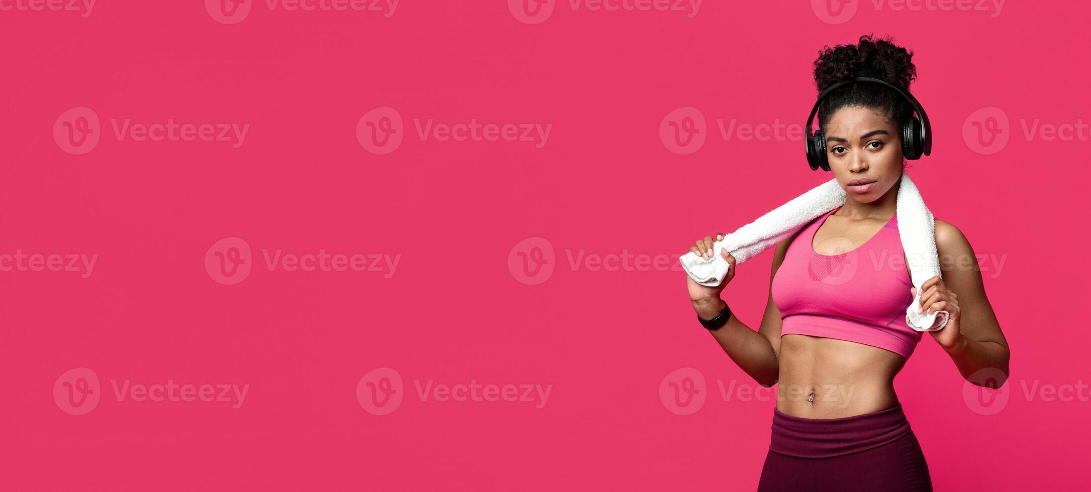Confident well fit afro girl with headset and towel on having break during training, red background, panorama with copy space photo