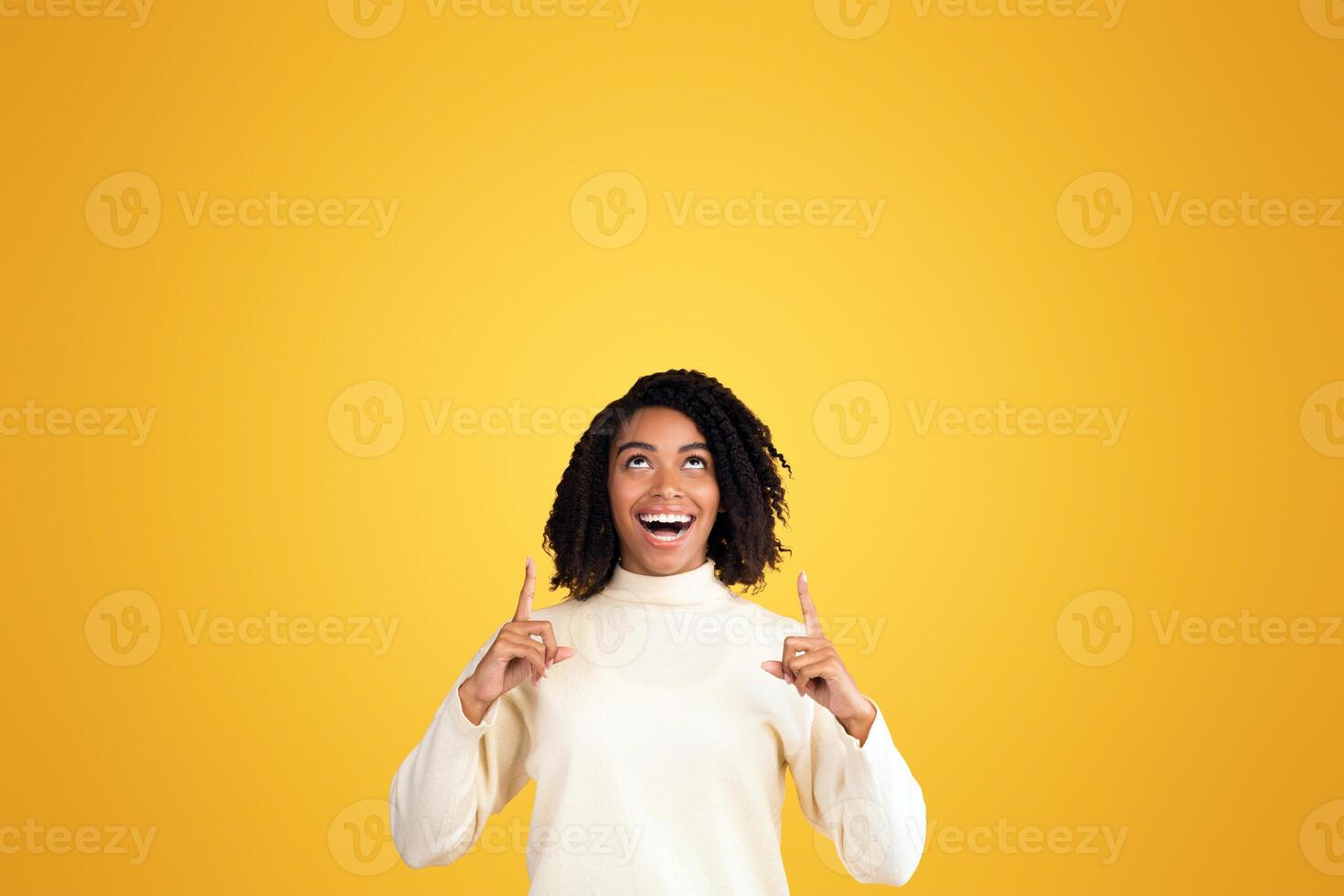 Place For Ad. Portrait of happy black girl pointing fingers up at copyspace isolated over yellow background, vertical image photo