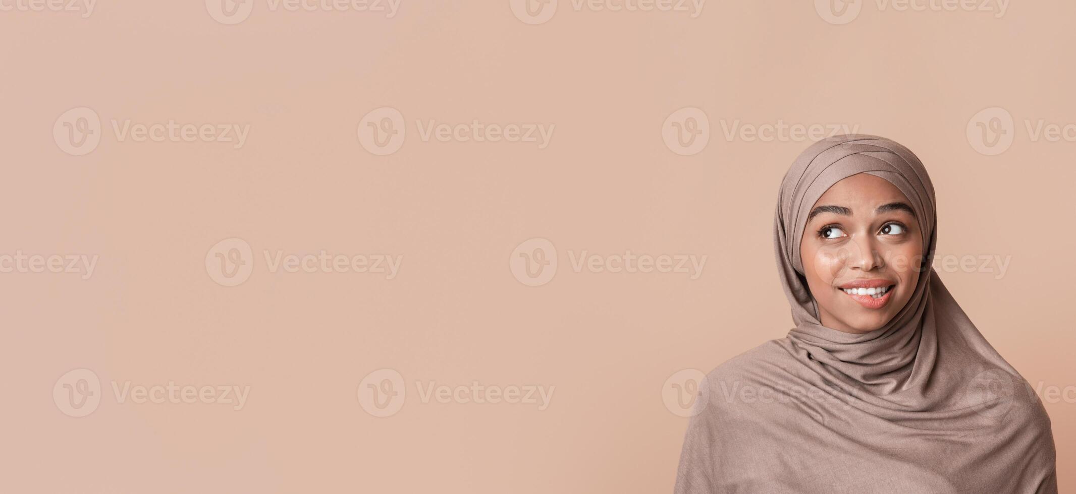 Portrait of doubtful black muslim woman in headscarf biting lip and looking away at free space over yellow background, unsure about something photo