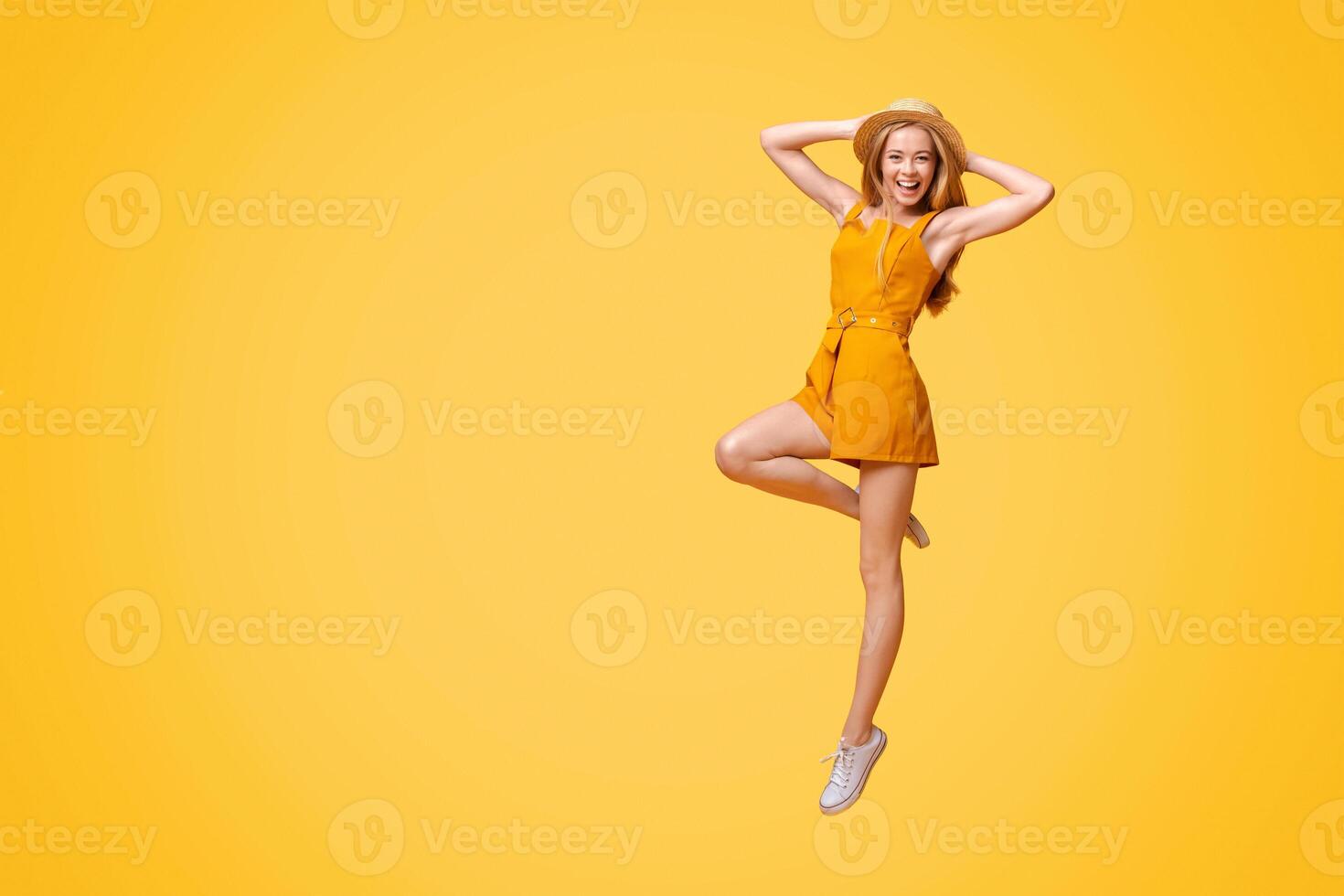 Summer Fashion. Joyful Teen Girl In Jumpsuit And Straw Hat Jumping On Yellow Studio Background With Copy Space photo