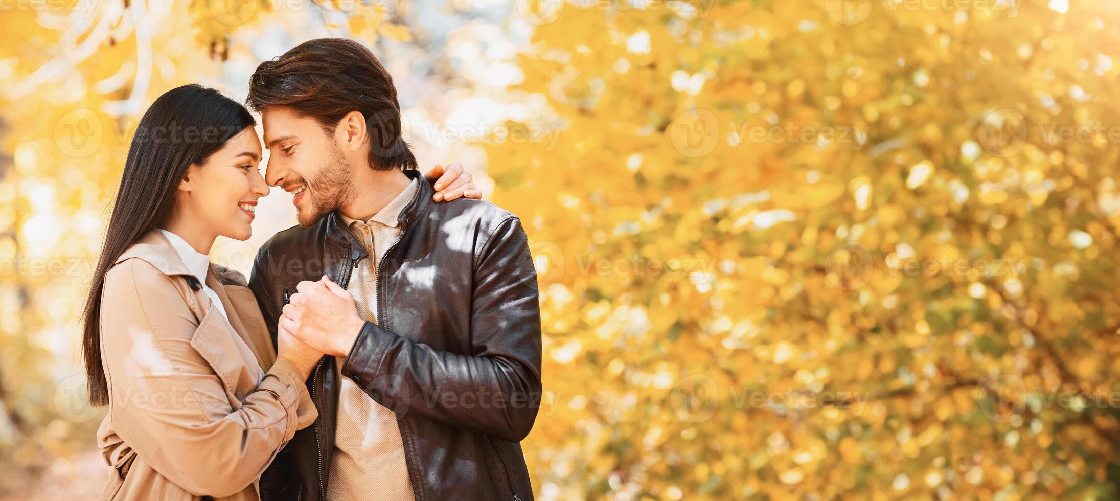 Couple embracing, holding hands and looking at each other over golden autumn trees, copy space photo