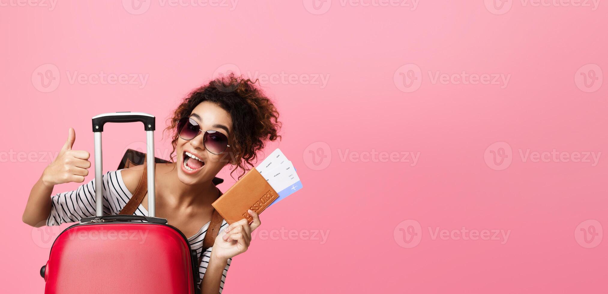 African American woman holding a red suitcase with one hand while giving a thumbs up gesture with the other hand. She appears happy and confident, copy space photo