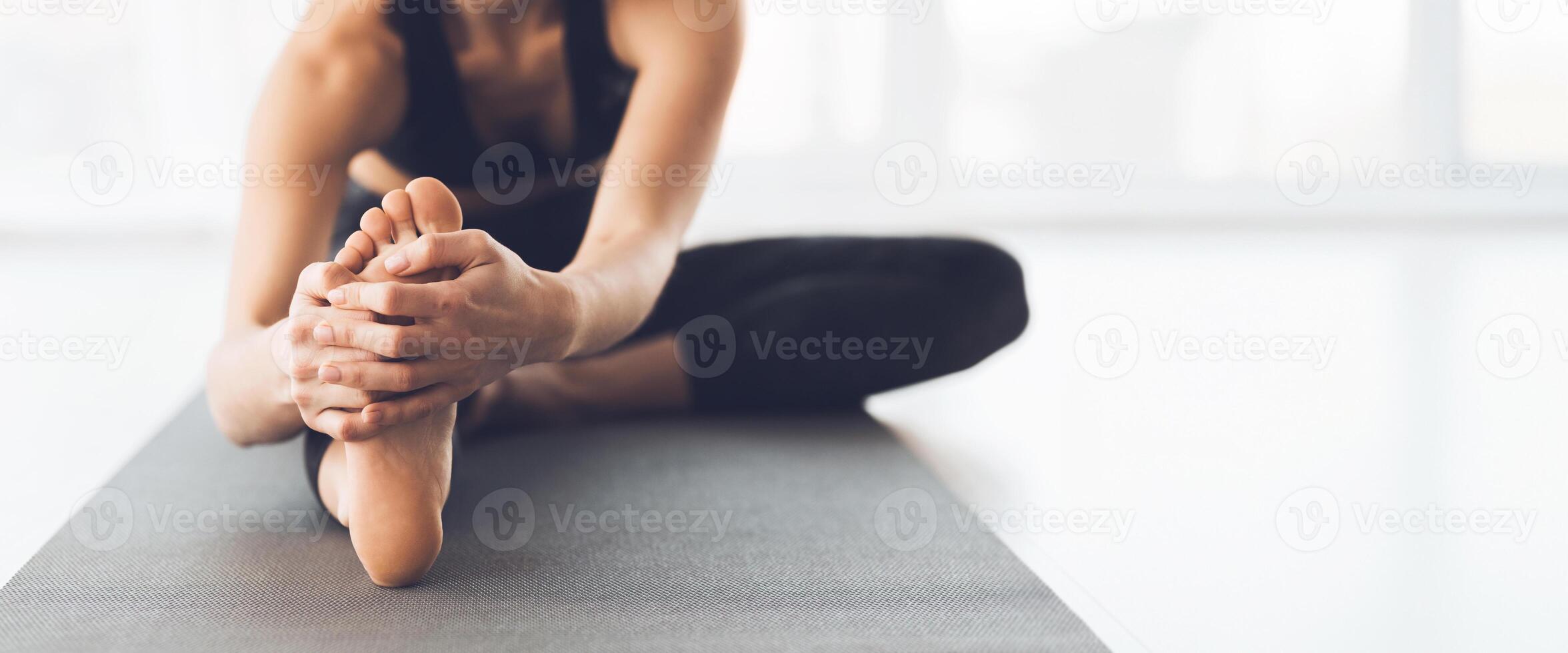 A person performs a seated toe stretch on a yoga mat in a well-lit studio, focusing on flexibility and relaxation, cropped, copy space photo