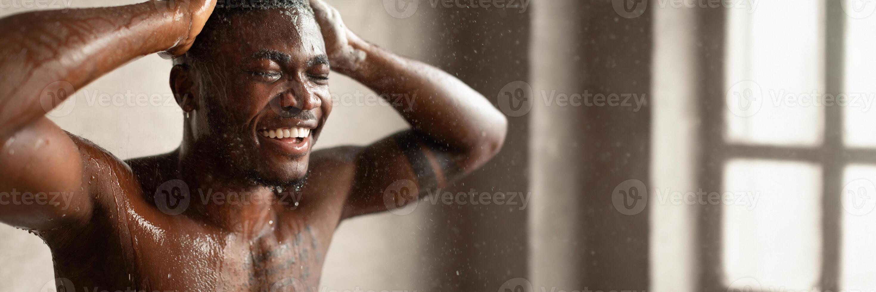 Black Man Taking Shower And Washing Head Standing With Eyes Closed Relaxing Under Hot Water In Bathroom Indoor. Hair And Body Care Concept. Selective Focus, Copy Space photo