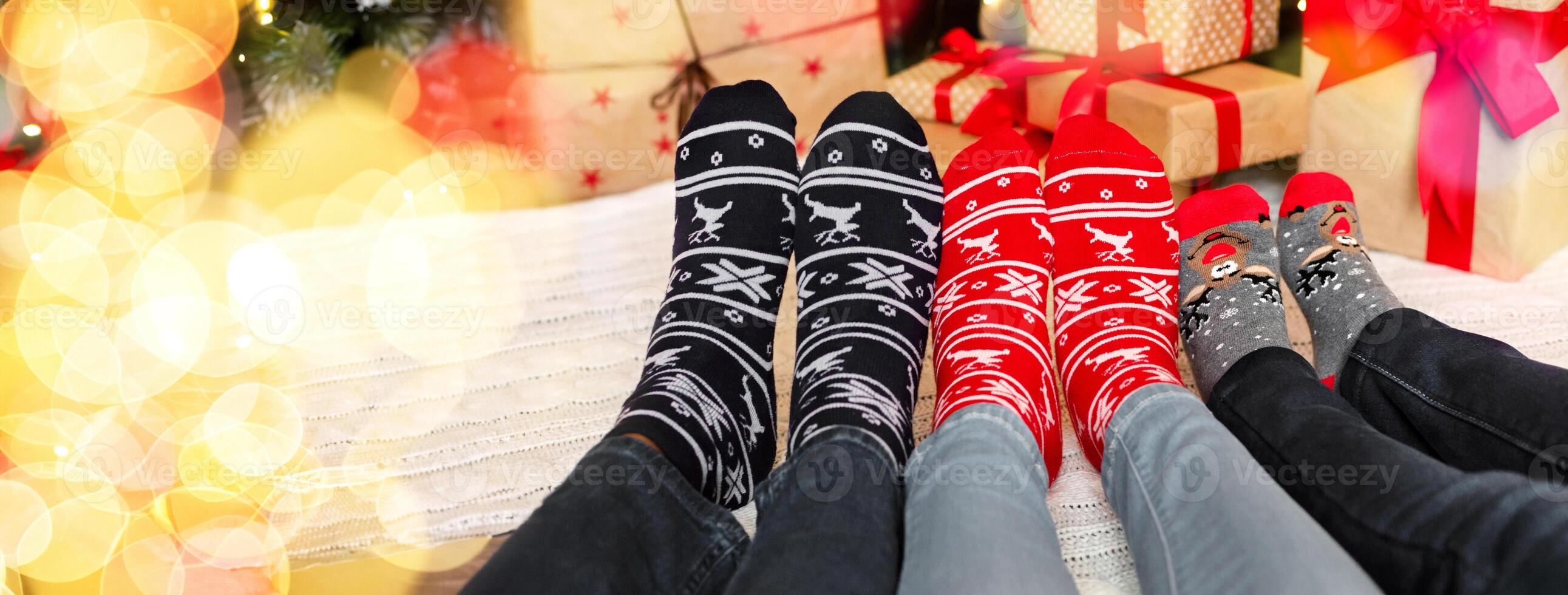 Christmas atmosphere background. Three pairs of feet in warm socks with winter holiday print ornament, panorama photo