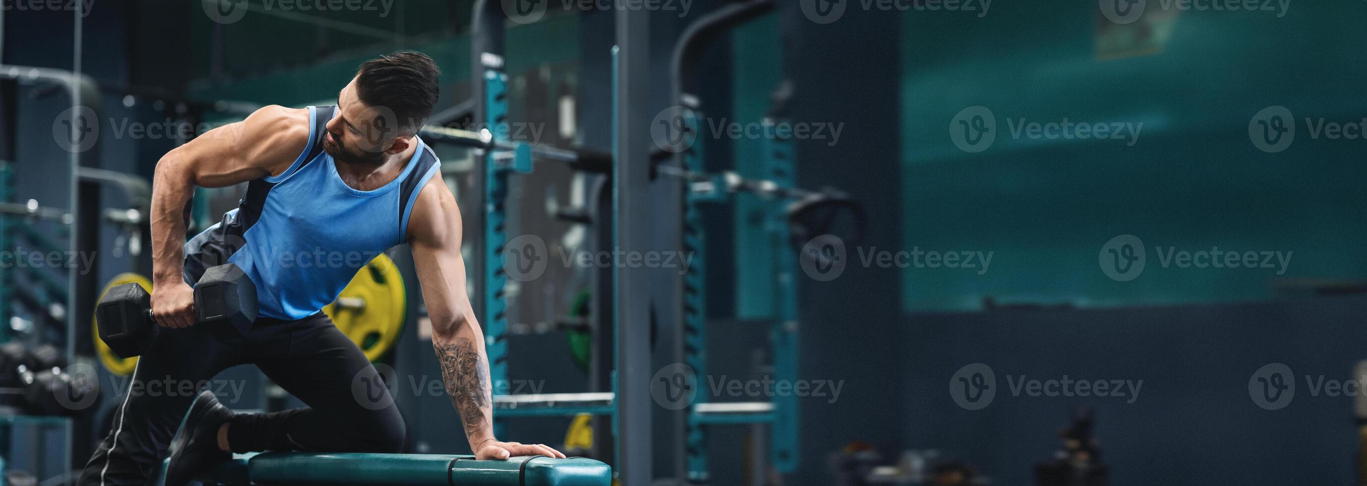 A man performs a strength training exercise with a dumbbell at a gym, focusing on building muscle and improving fitness, copy space photo