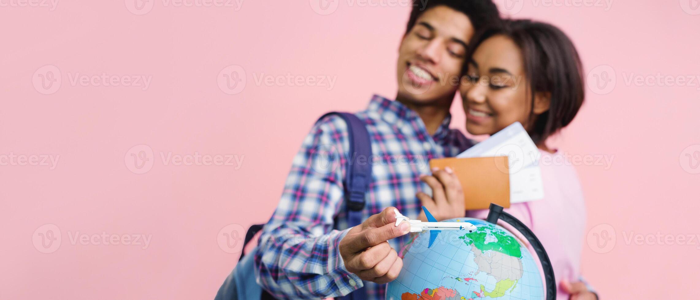 Happy teen couple preparing for trip with globe, girl holding passport and tickets on pink background photo