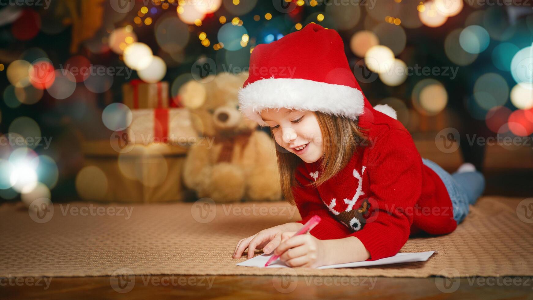 Cute little girl in red hat laying on floor and writing letter to Santa, copy space photo