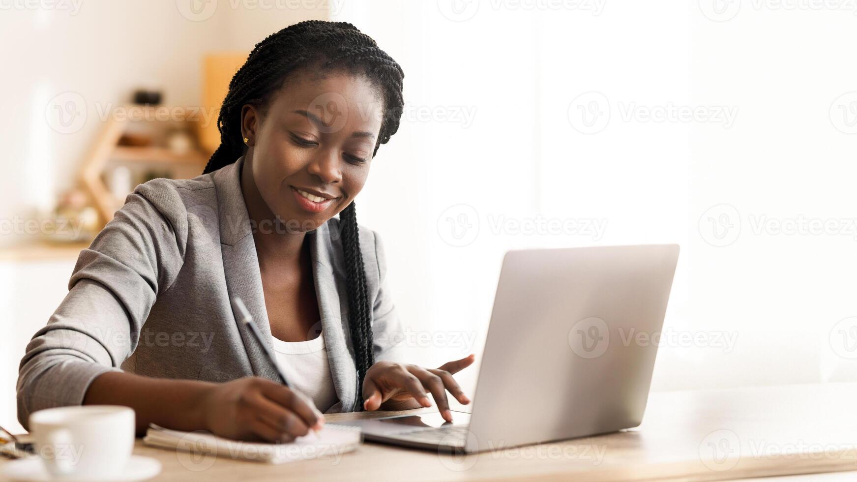 Black female entrepreneur working in office, typing on laptop computer and taking notes, free space photo