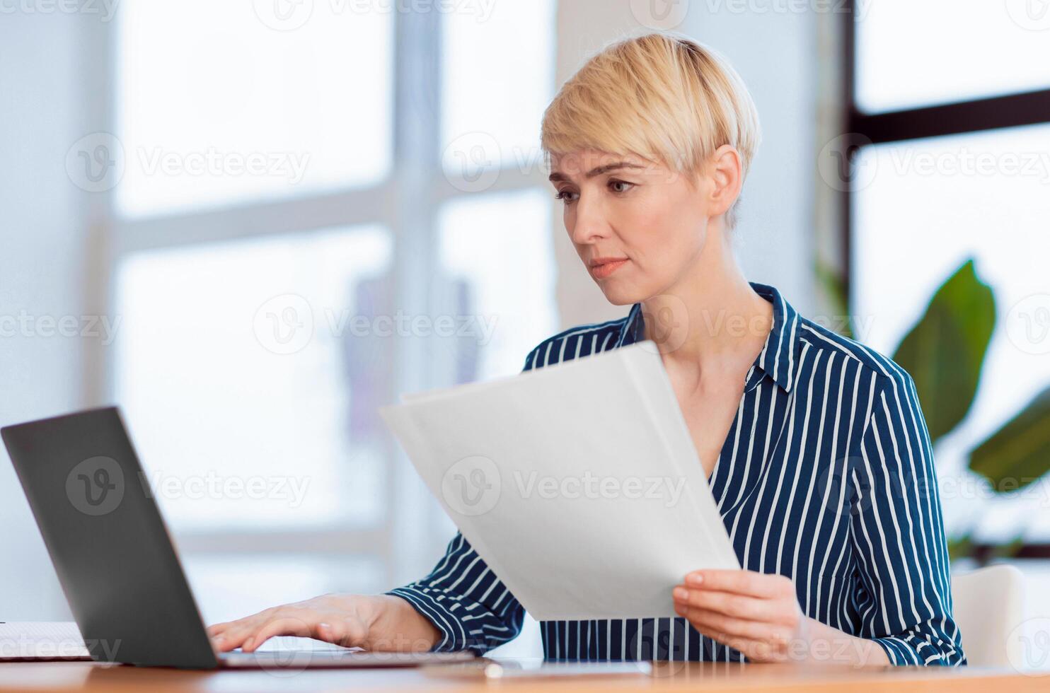 Busy Entrepreneur Woman Working On Laptop Holding Papers And Business Reports Sitting In Modern Office. Selective Focus photo