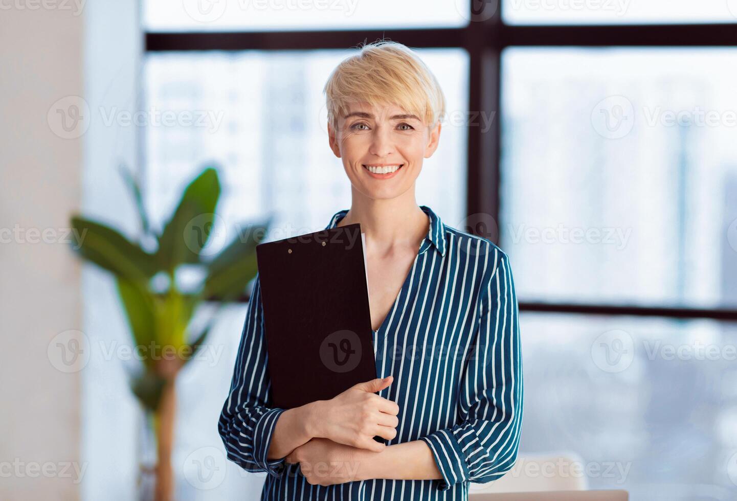 Middle-Aged Entrepreneur Lady Holding Folder Smiling At Camera Standing Near Window In Office. Business Career Concept photo