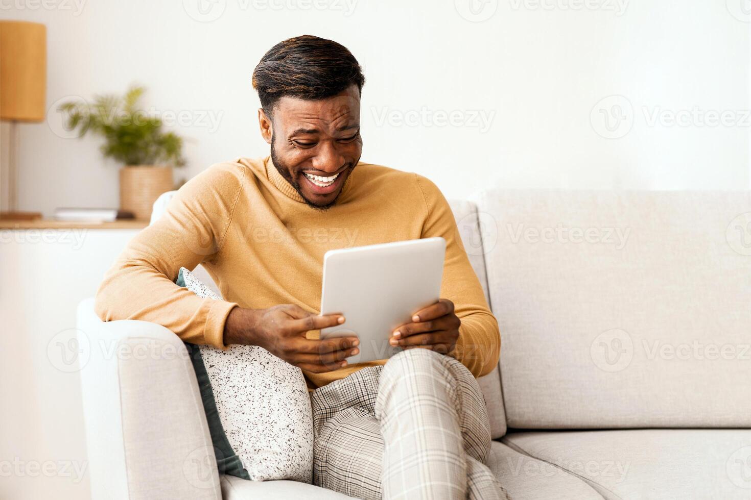 Positive African American Man Using Digital Tablet Laughing Watching Funny Comedy Movie Sitting On Sofa Indoor. Selective Focus photo