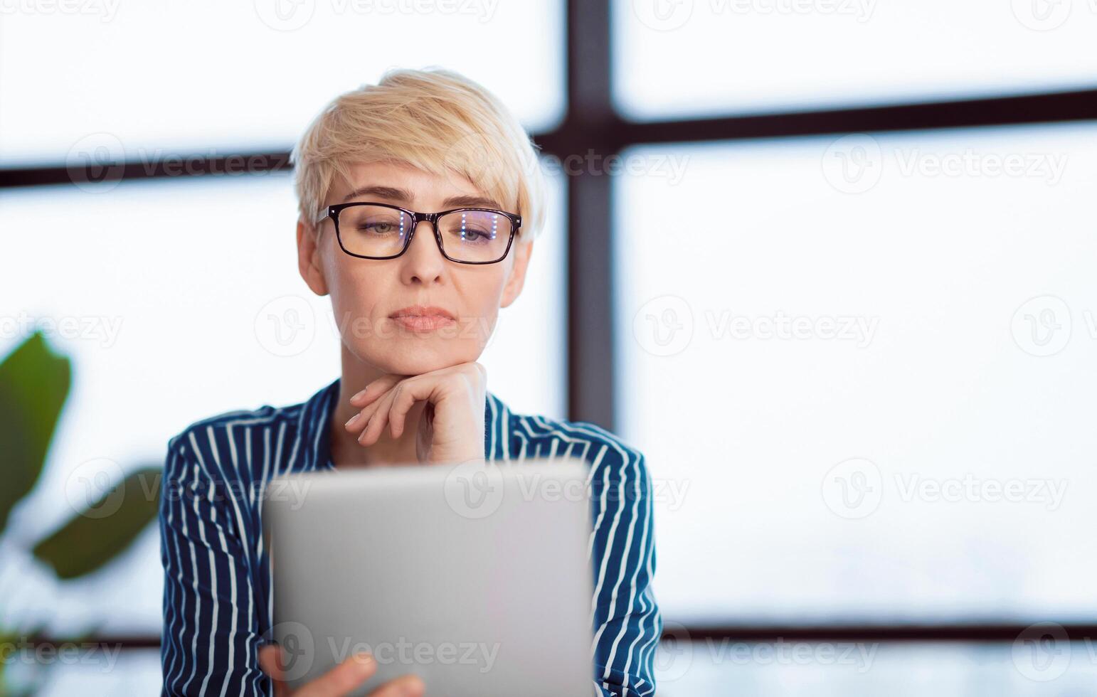 Lady Using Digital Tablet Reading Business News Sitting Against Window In Modern Office. Copy Space, Selective Focus photo