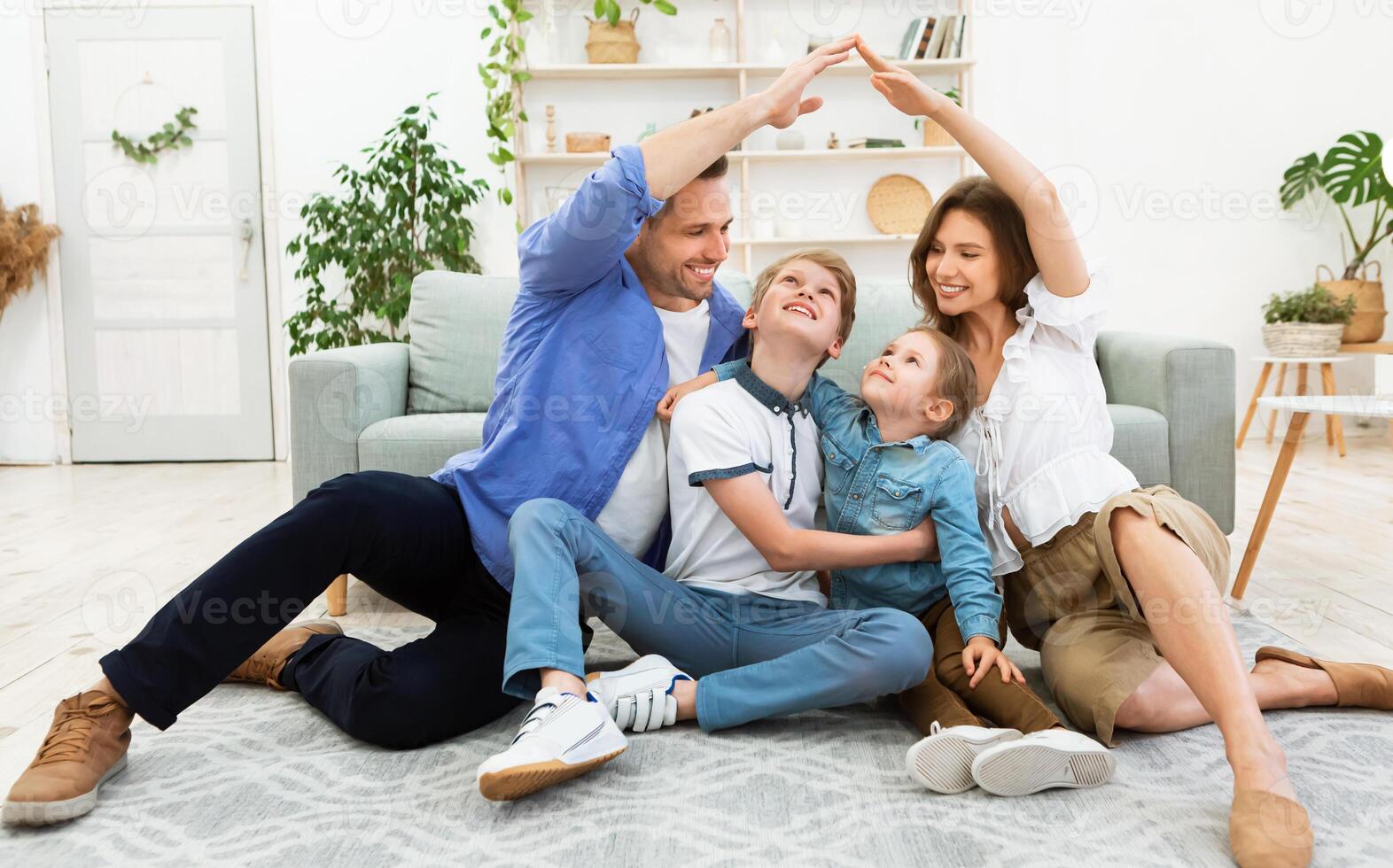 Housing for family. Young parents joining hands making symbolic house roof sitting with children on floor in new apartment. photo