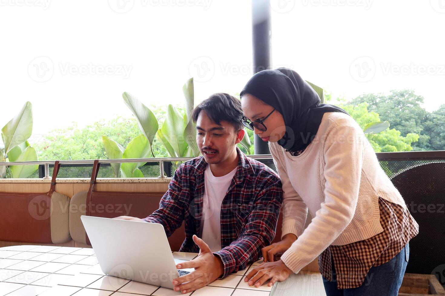 Two Young Asian Working People, Discussing at the Cafe Table, Working with Laptop Explaining File on Screen photo