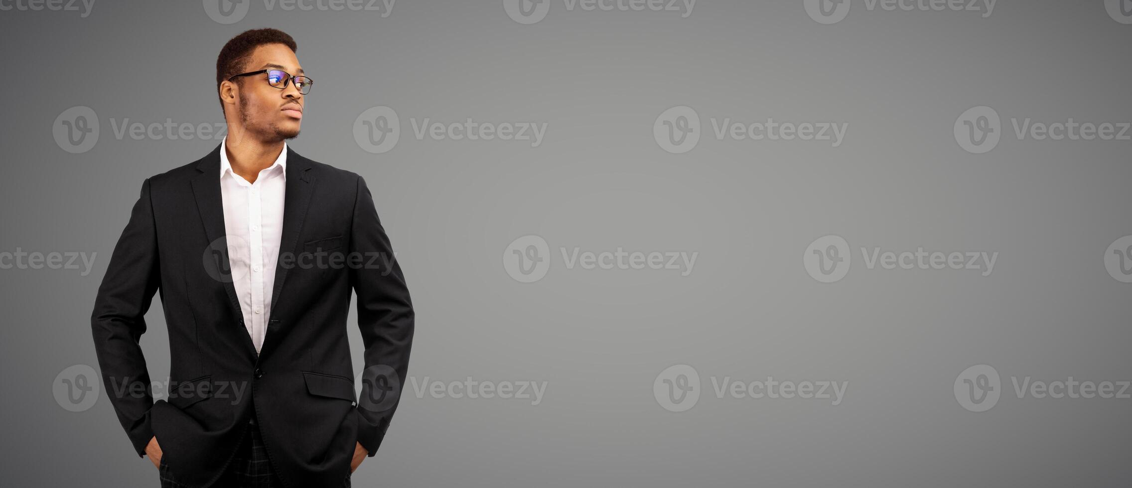 Young black businessman with hands in his pockets looking aside, white studio background with copyspace photo