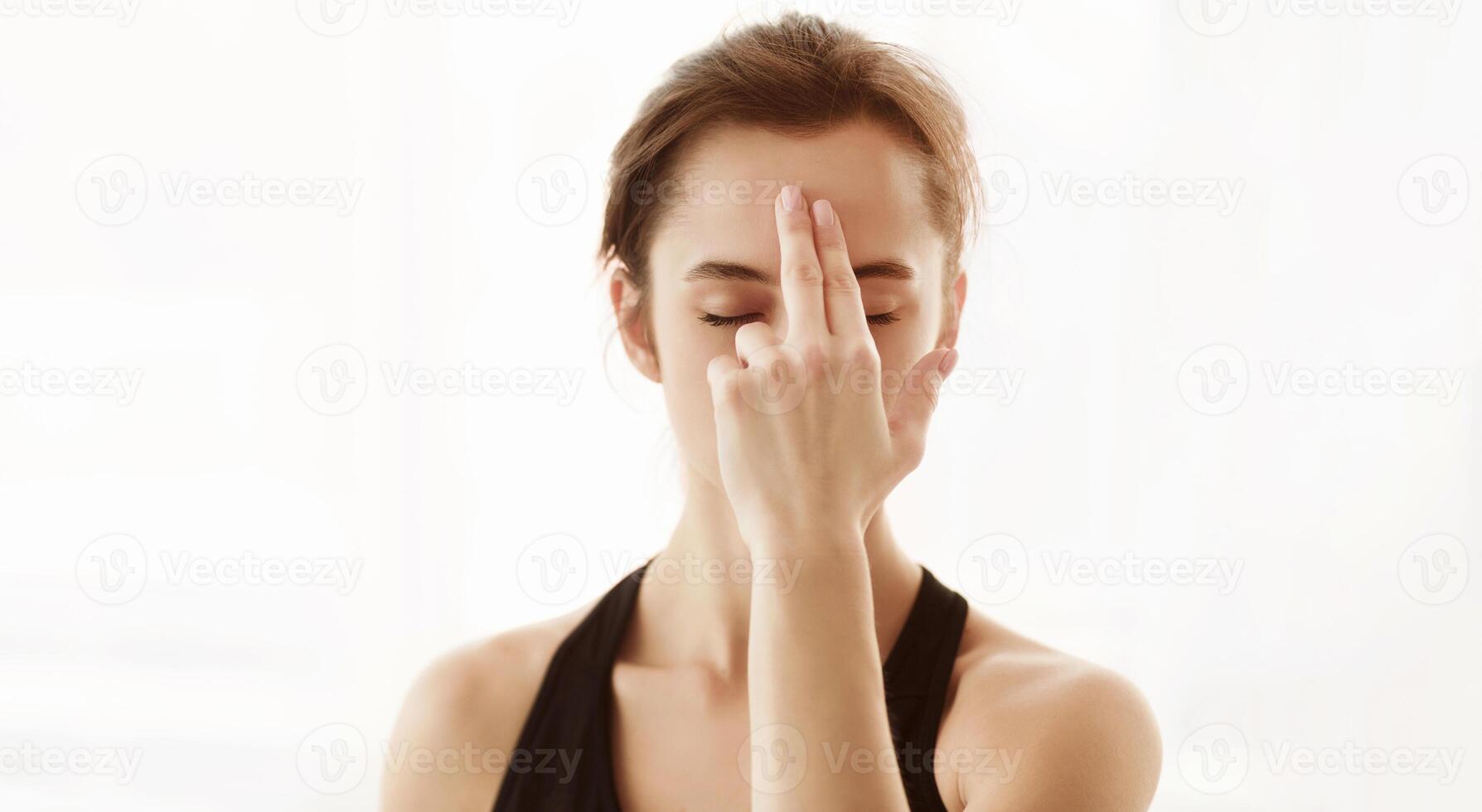 A young woman is practicing yoga inside a serene, softly lit room. She is performing a breathing exercise with her eyes closed, focusing on her inner peace. photo