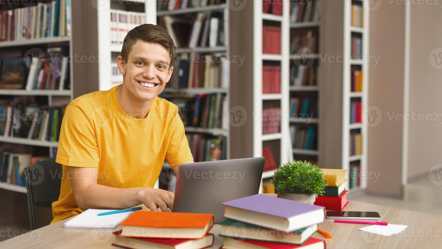Intelligent guy studying in school library, using laptop and searching for information on internet, copy space photo