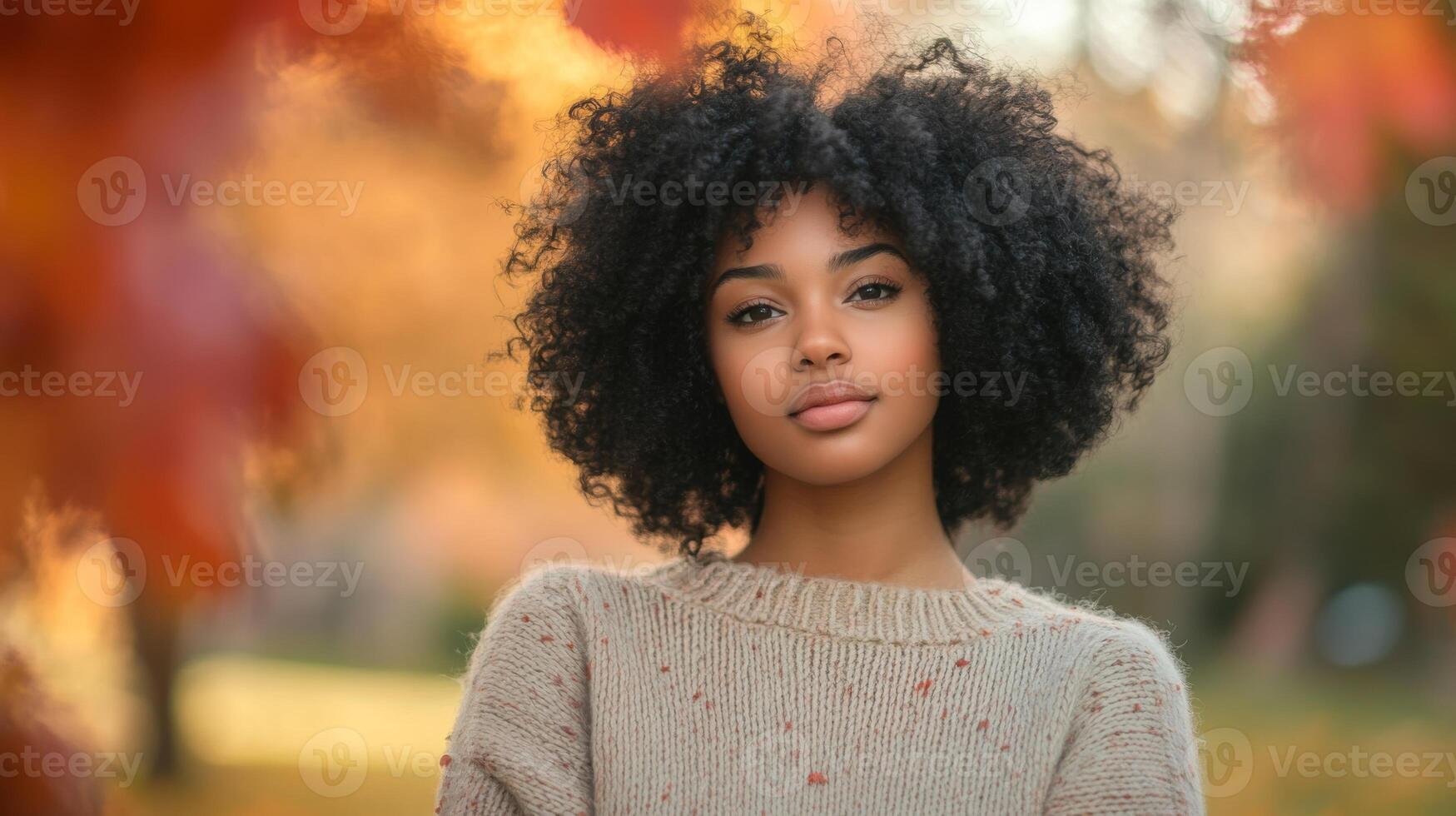A young woman stands confidently in a cozy sweater as colorful autumn leaves frame her in a serene park. The warm glow of the golden hour highlights her natural beauty and relaxed expression. photo