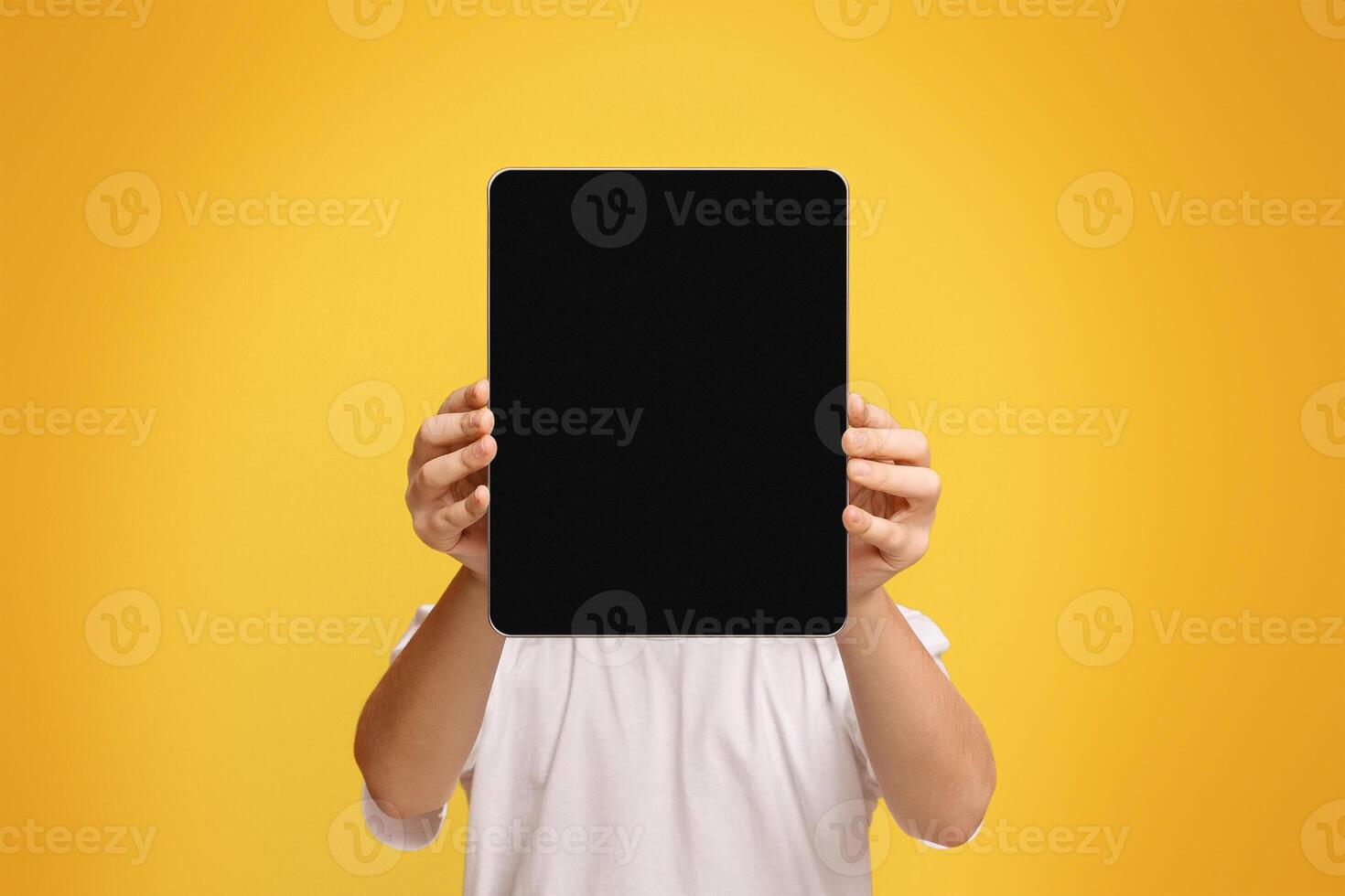 Tablet face. Little boy hiding his face behind portable computer device on orange background, free space photo