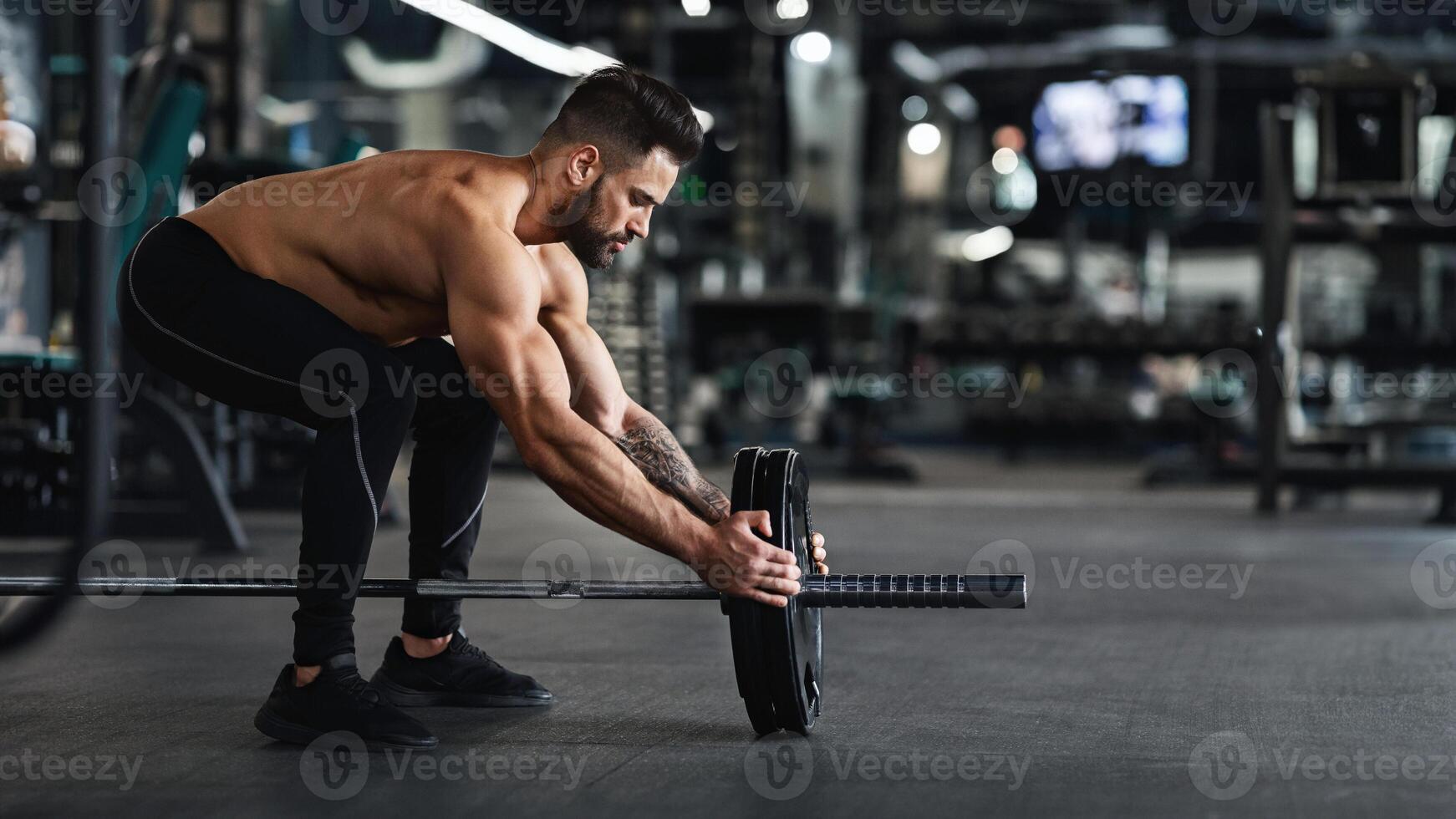 Athlete adding weight plates on his barbell, preparing for his weightlifting workout at gym, free space photo