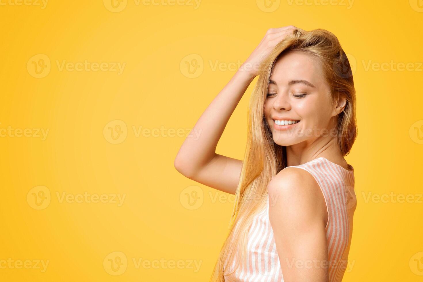 adolescente belleza. linda joven niña disfrutando conmovedor su hermosa rubio cabello, posando terminado amarillo fondo, de cerca retrato foto
