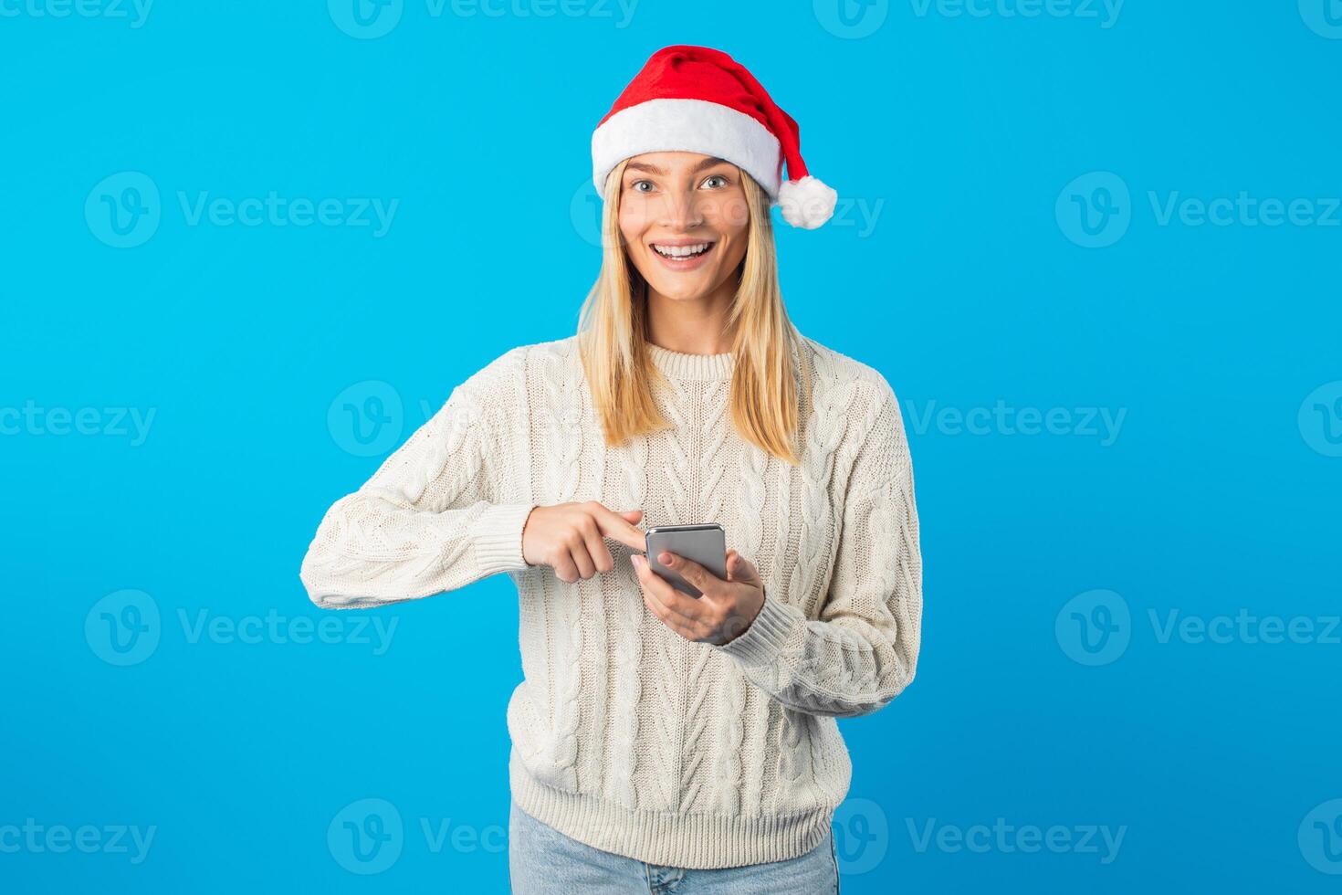 A woman wearing a Santa hat is holding a cell phone in her hand, looking at the screen. She appears to be checking a message or browsing content on the device. photo