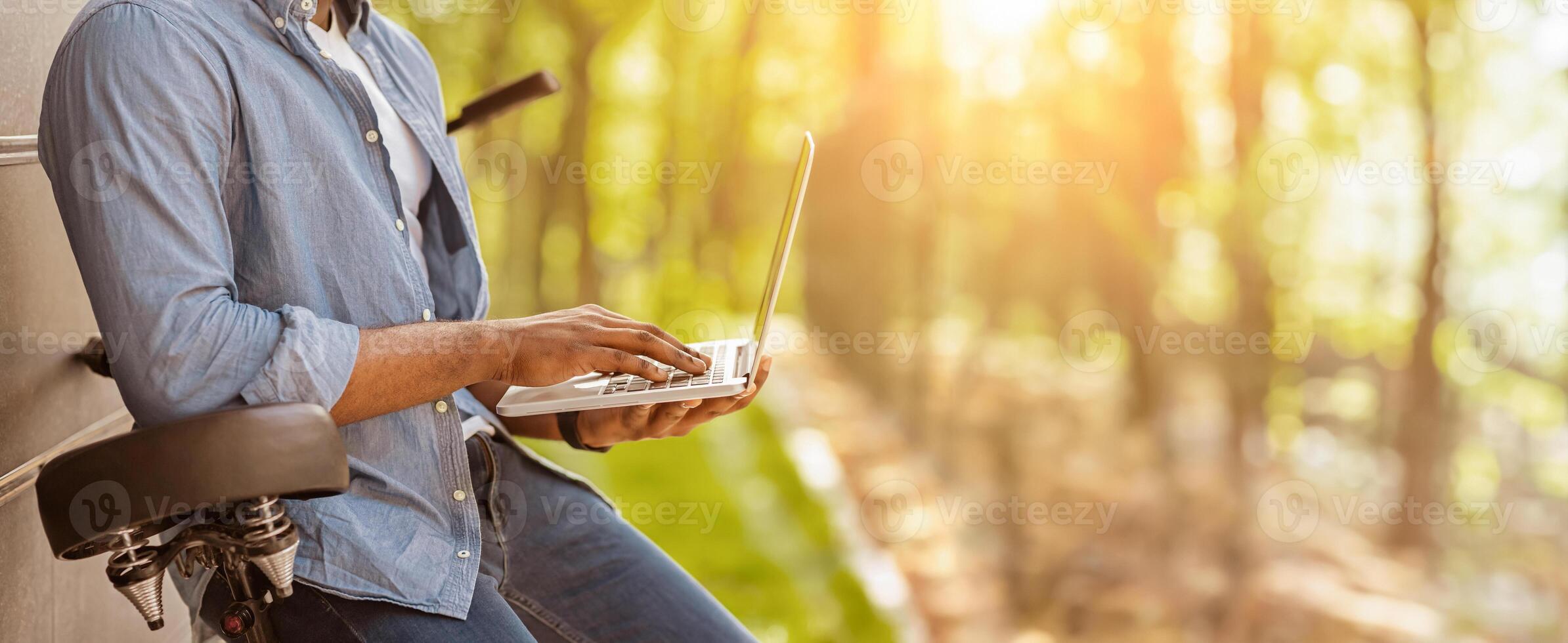 Unrecognizable black man leaning on bicycle and using laptop outdoors, side view, cropped image with free space photo