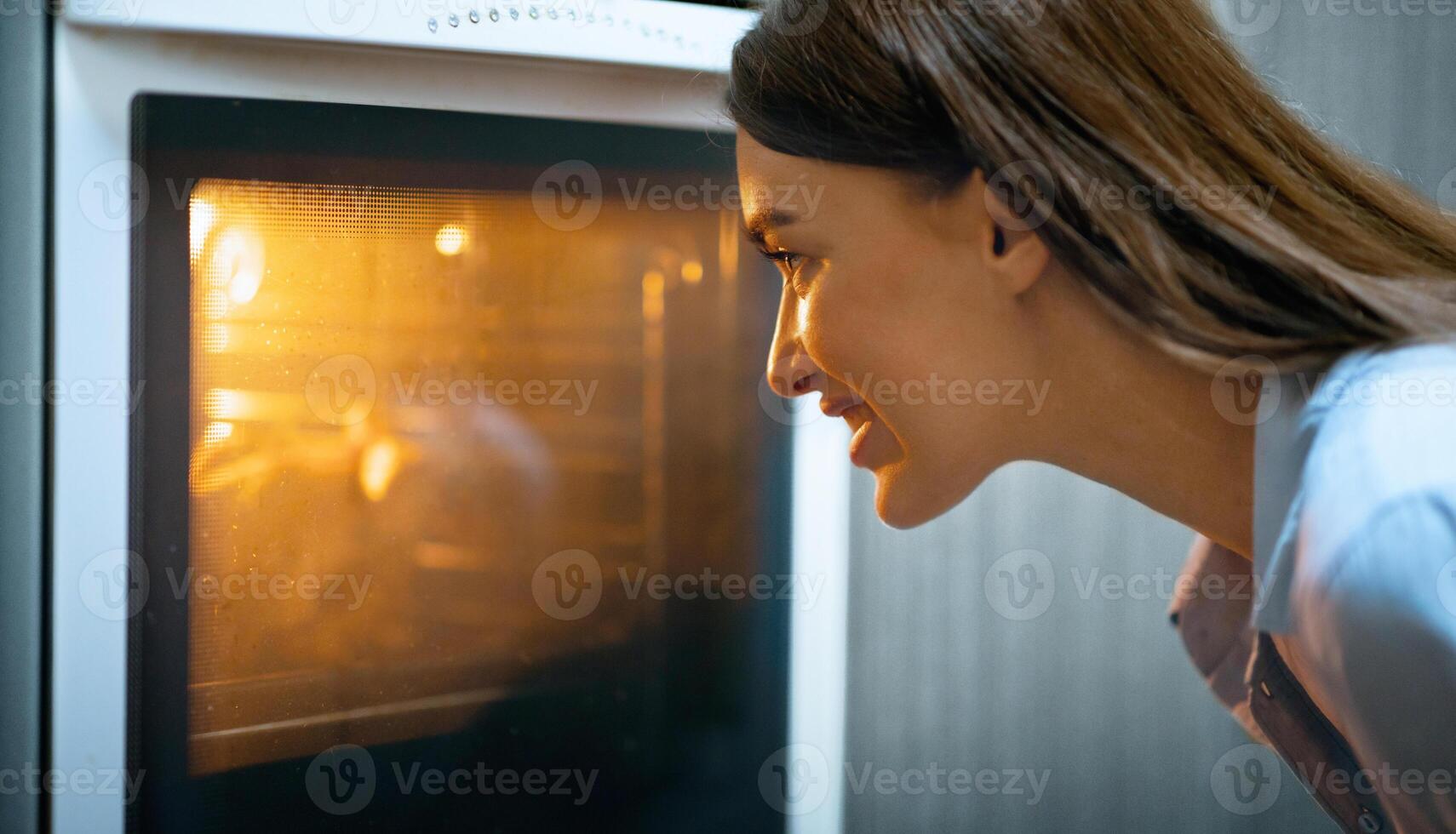 Homemade grill. Young housewife watching her lunch in oven at kitchen, free space photo