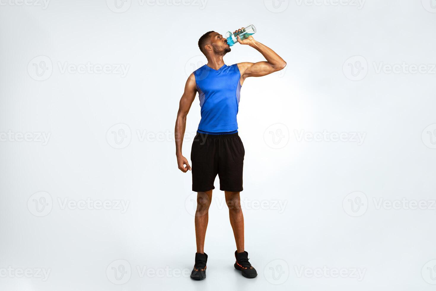Stay Hydrated. Full length muscular afro man drinking water from bottle over yellow studio background, copyspace photo