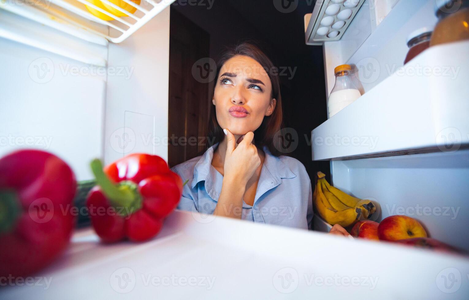 What should I eat. Young pensive woman thinking near opened fridge, view from inside photo