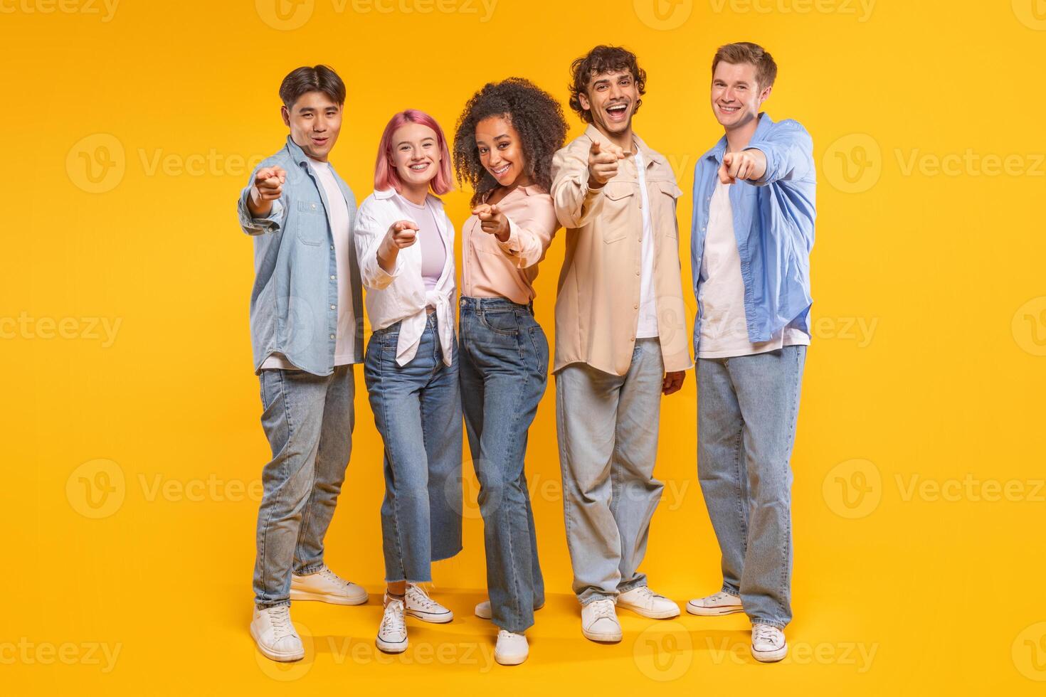 Five young adults stand in a line, pointing their index fingers toward the camera. They all smile at the camera, exuding a sense of camaraderie and unity. photo